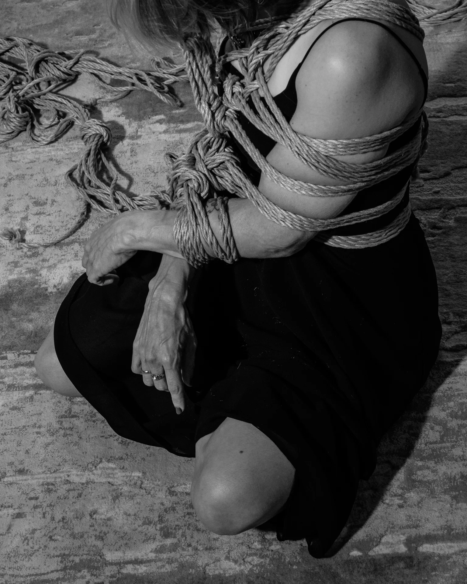 Close view of hands and rope over a black dress; the face is outside the frame.