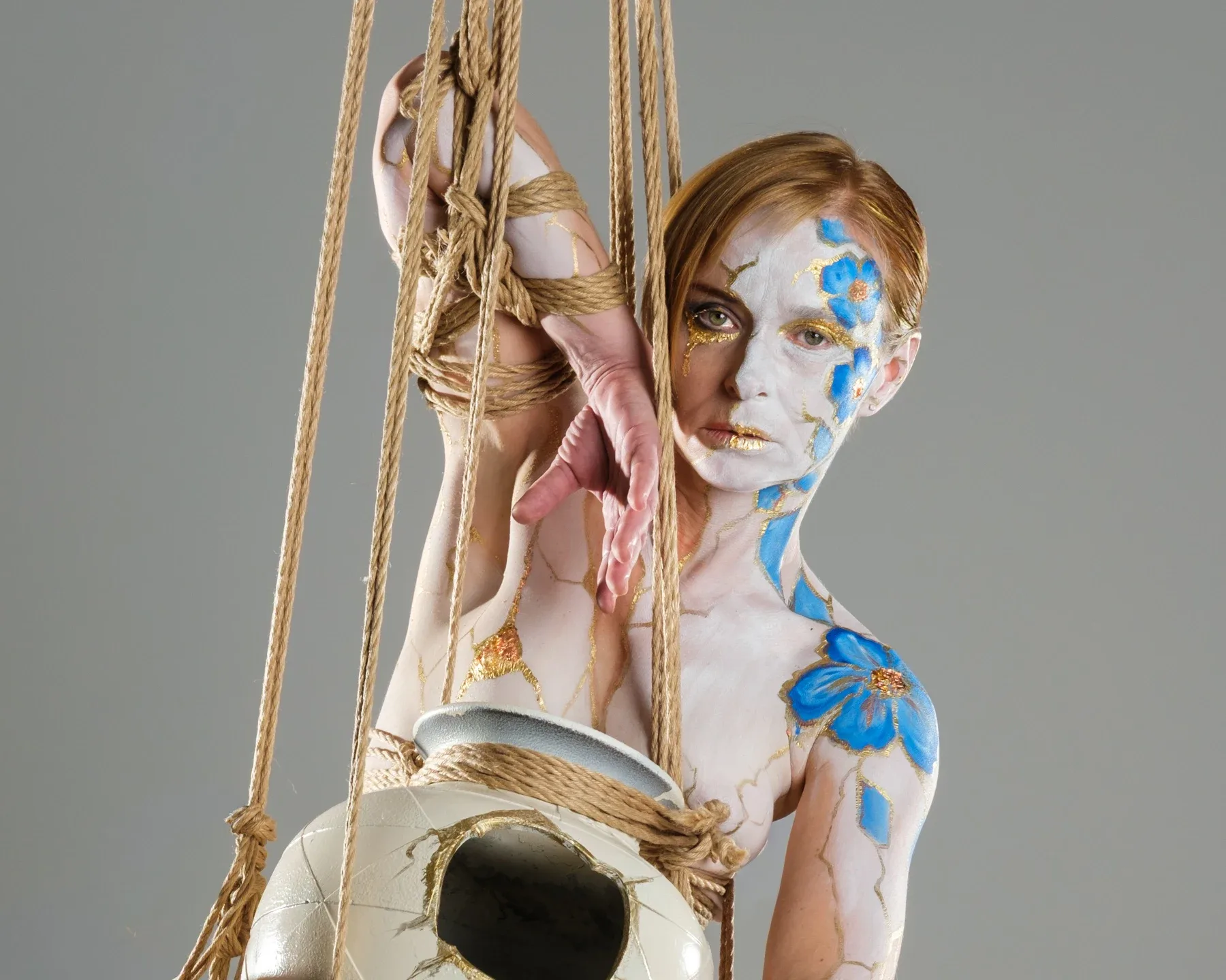 Tiana looks directly at the camera through vertical ropes, with her bound hands raised and the vessel partly visible below.
