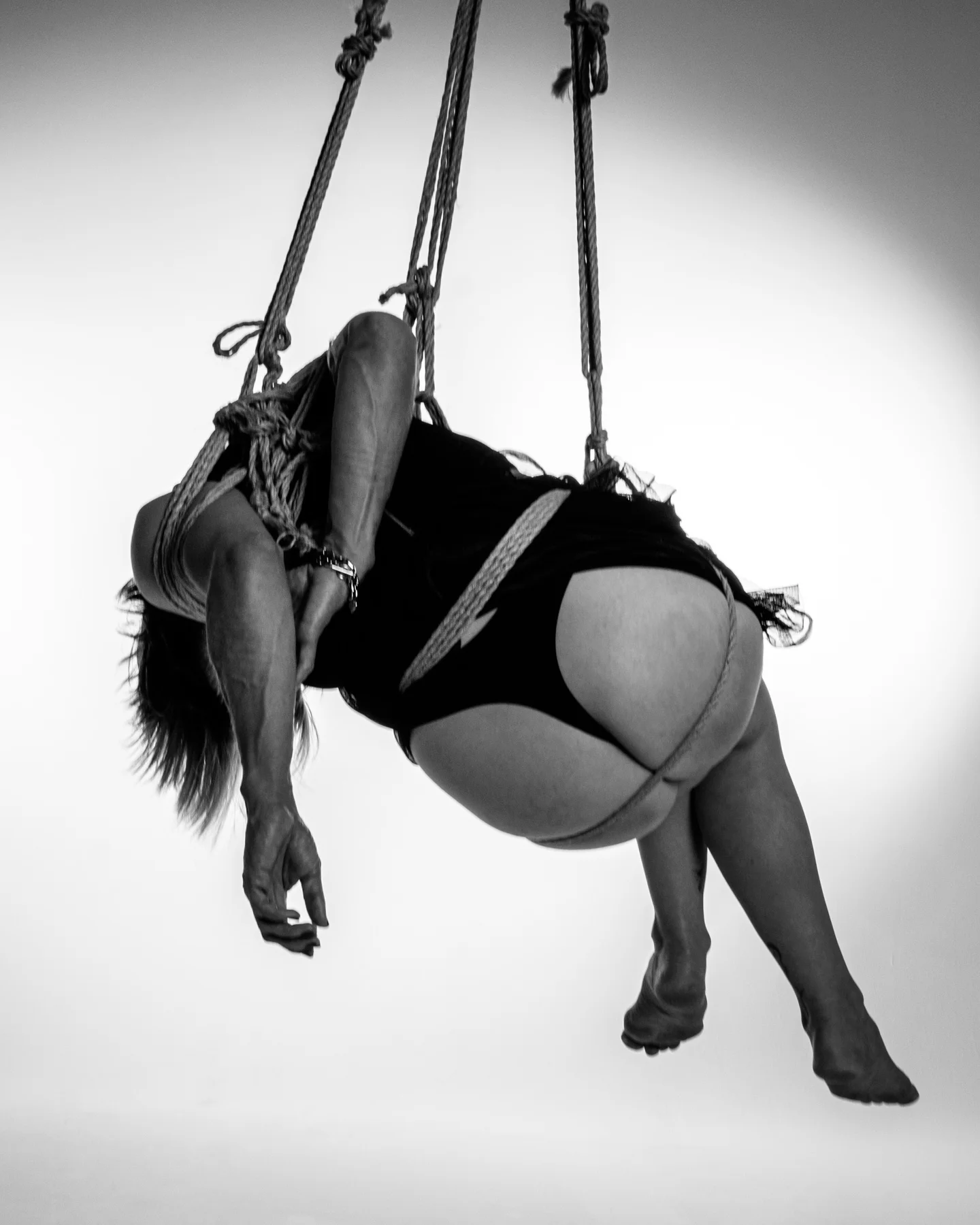 A curved figure suspended against a light background, her face hidden by her hair.