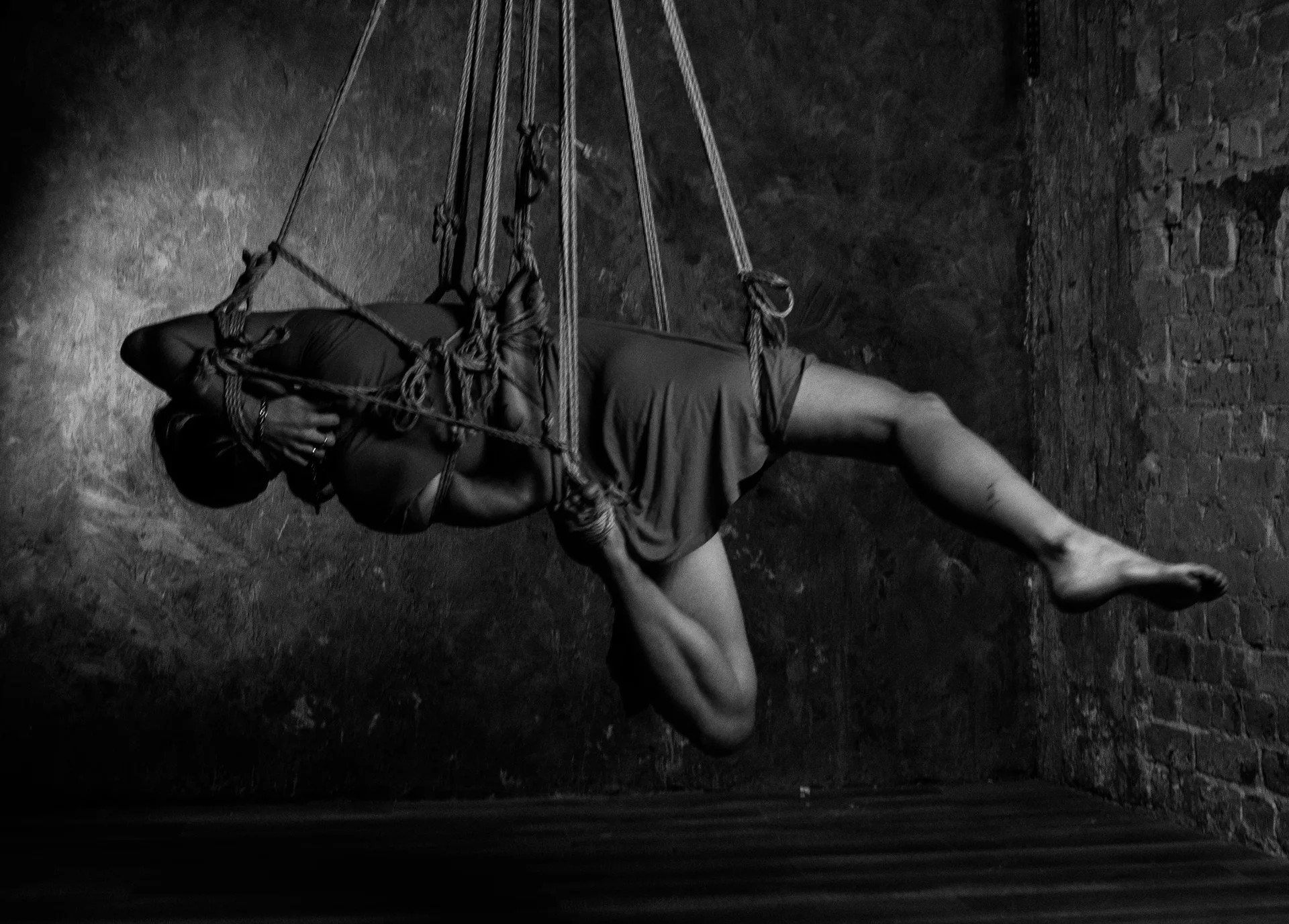 A horizontal figure in a dress against a dark, textured wall.