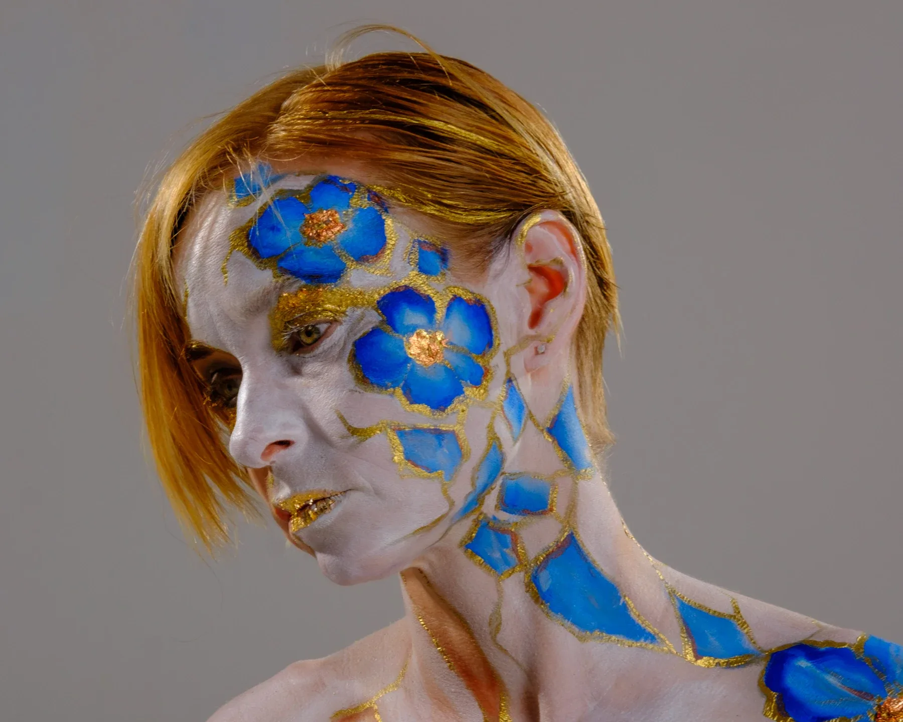 Close portrait of Tiana looking down; blue flowers and gold branching lines cover her face, neck and shoulder.