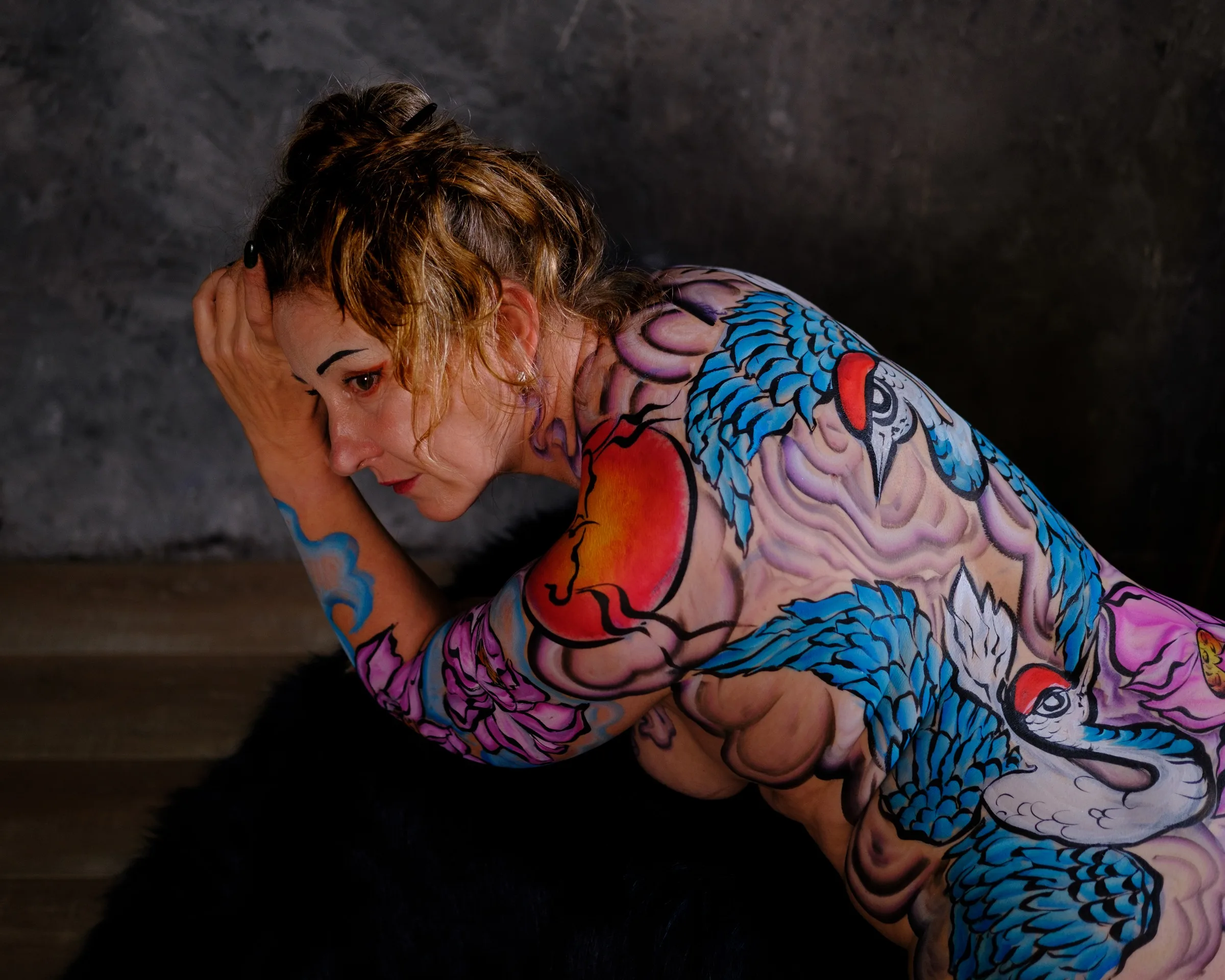 A seated figure folds inward, bringing the painted cranes and peonies close to the face.