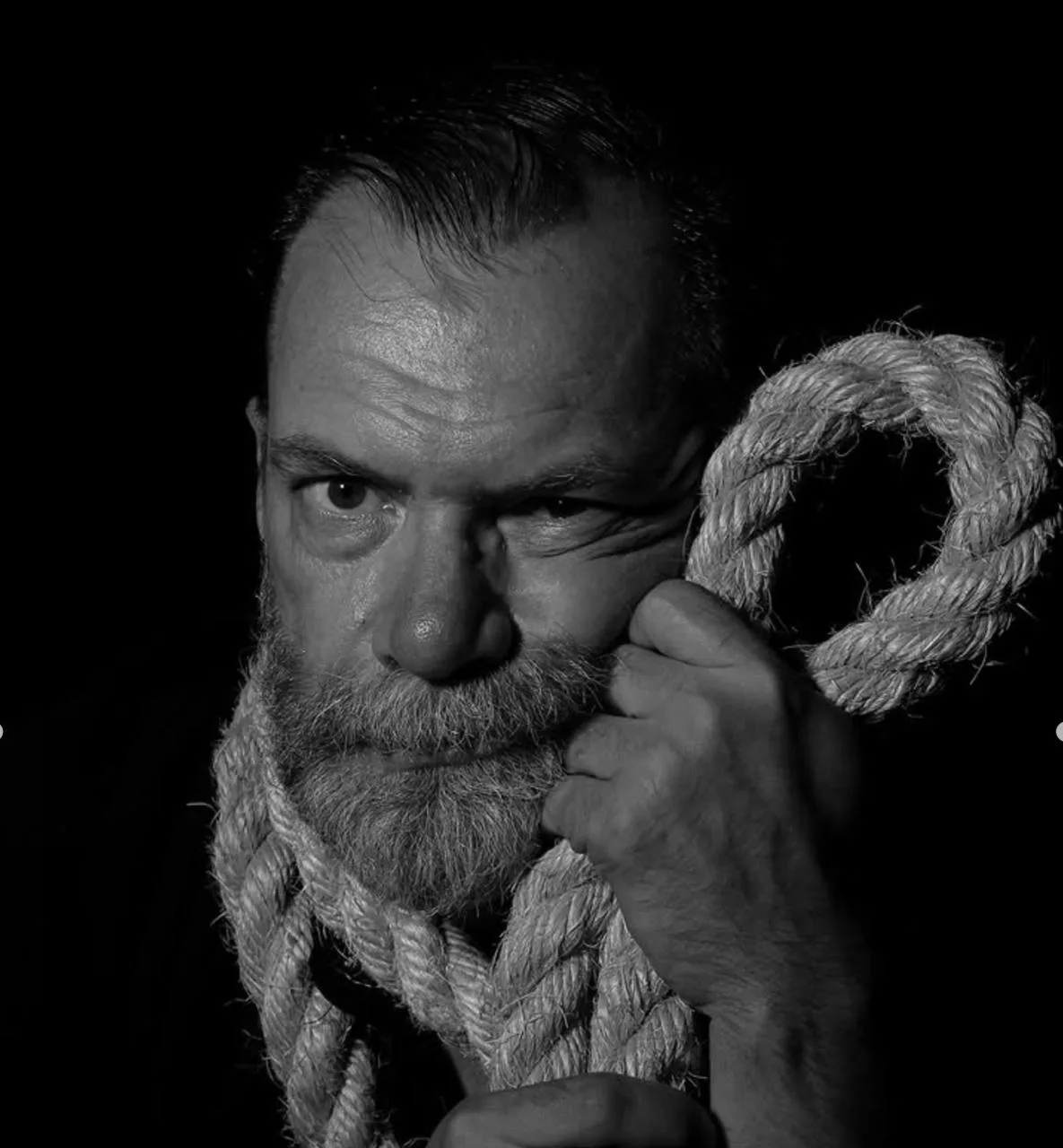 Black-and-white portrait of Roman / Ded Mazai holding a thick rope.