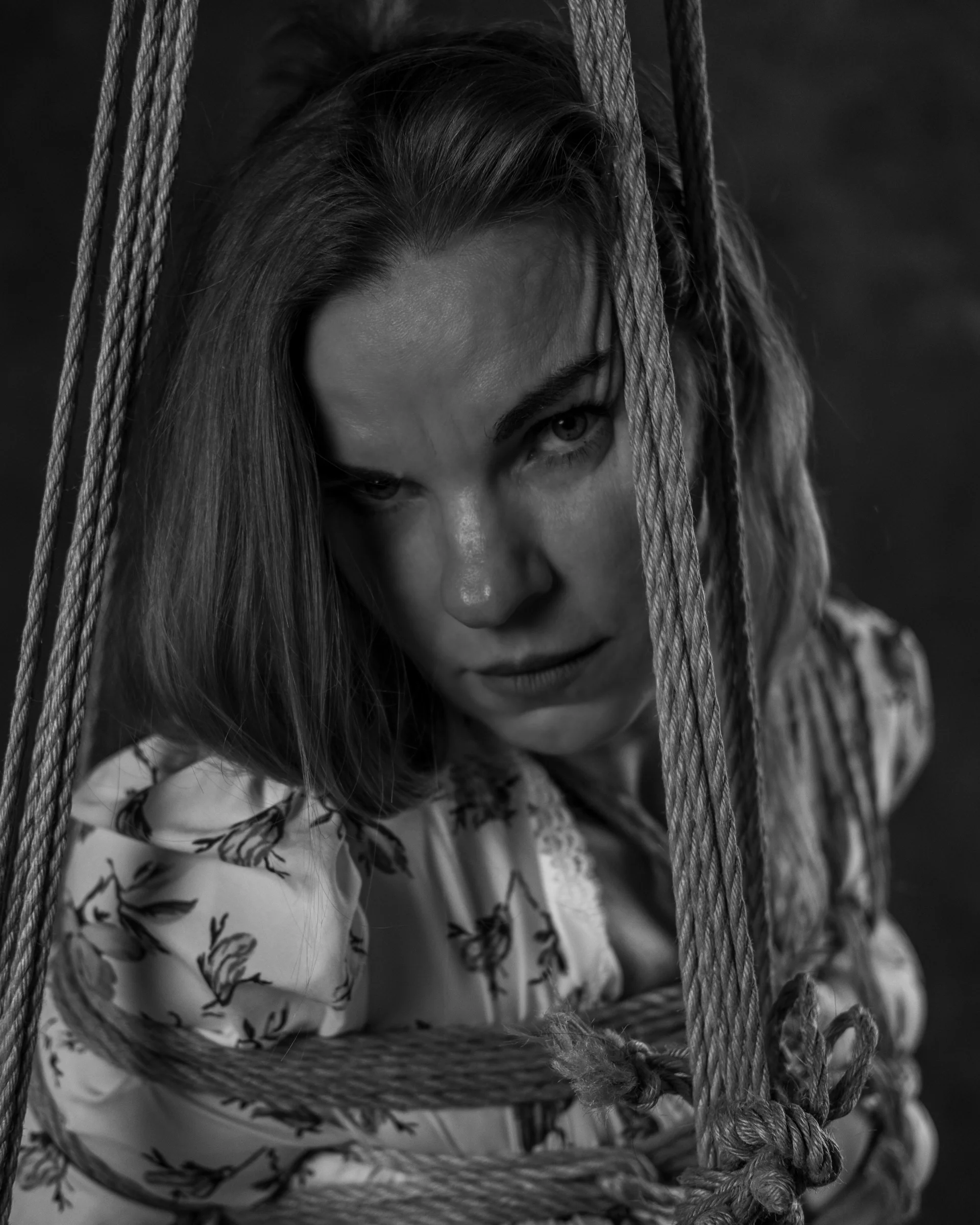 Black-and-white portrait with a direct gaze between lines of rope.