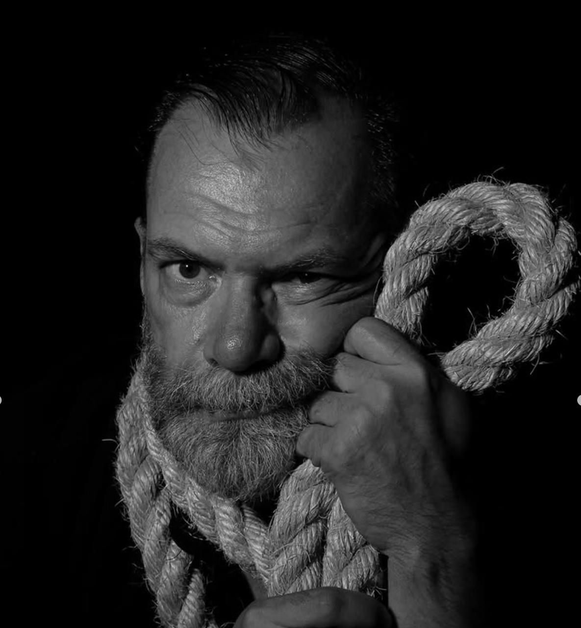 Black-and-white portrait of Roman / Ded Mazai holding a thick rope.
